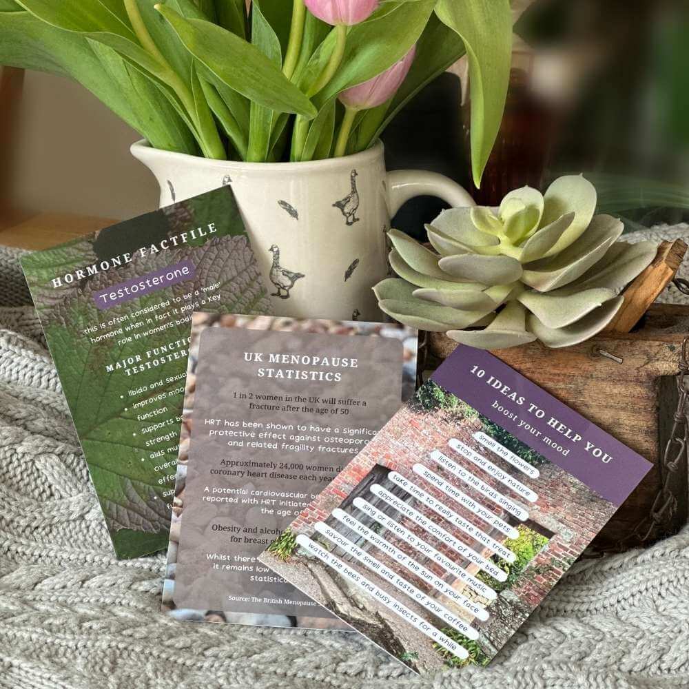 A still life shot of 3 better menopause cards leaning against a vase of tulips on a textured light grey surface. The cards show a hormone fact file card on testosterone, a UK Menopause statistics card and a card with 10 ideas to help you boost your mood.