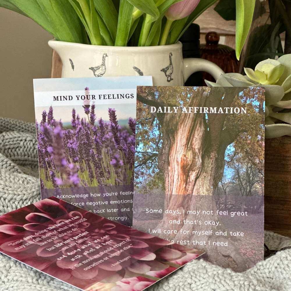 A still life photo showing a close up of 3 better menopause cards leaning against a vase. One is titled 'Mind your feelings' and is about acknowledging how you're feeling rather than forcing your feelings down. The other shows a daily affirmation and one has a quote on it.